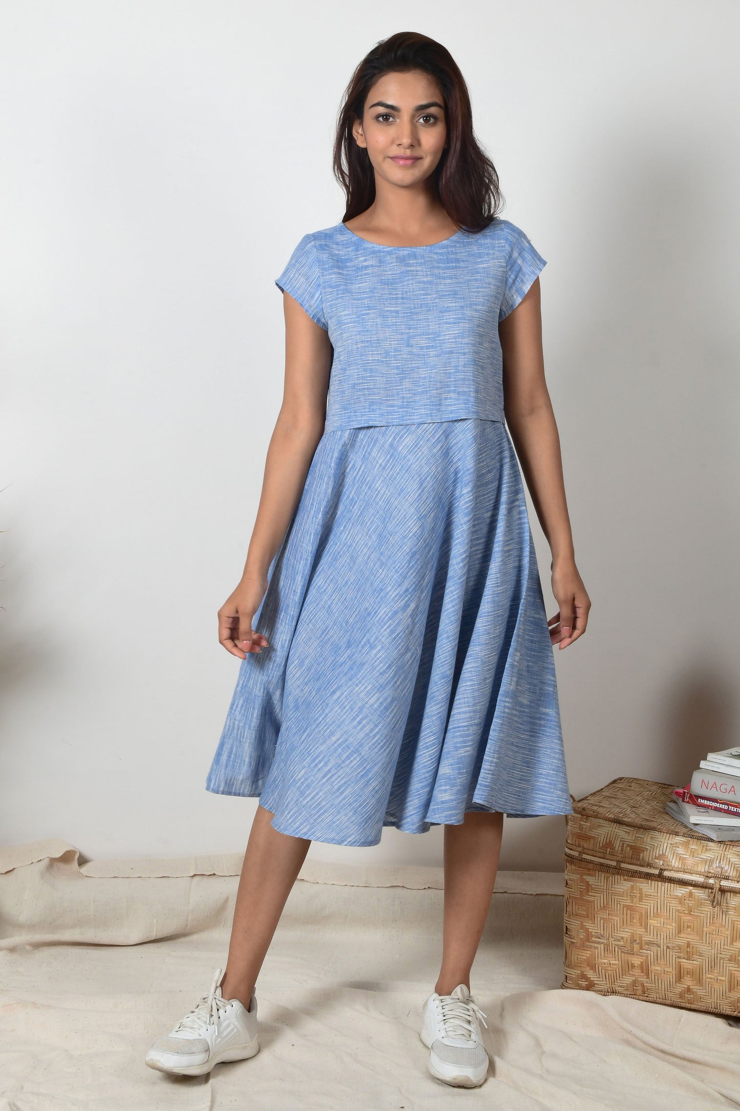 Indian girl with black hair and white sneakers wearing a blue a-line dress made with cotton that hand spun and hand woven.