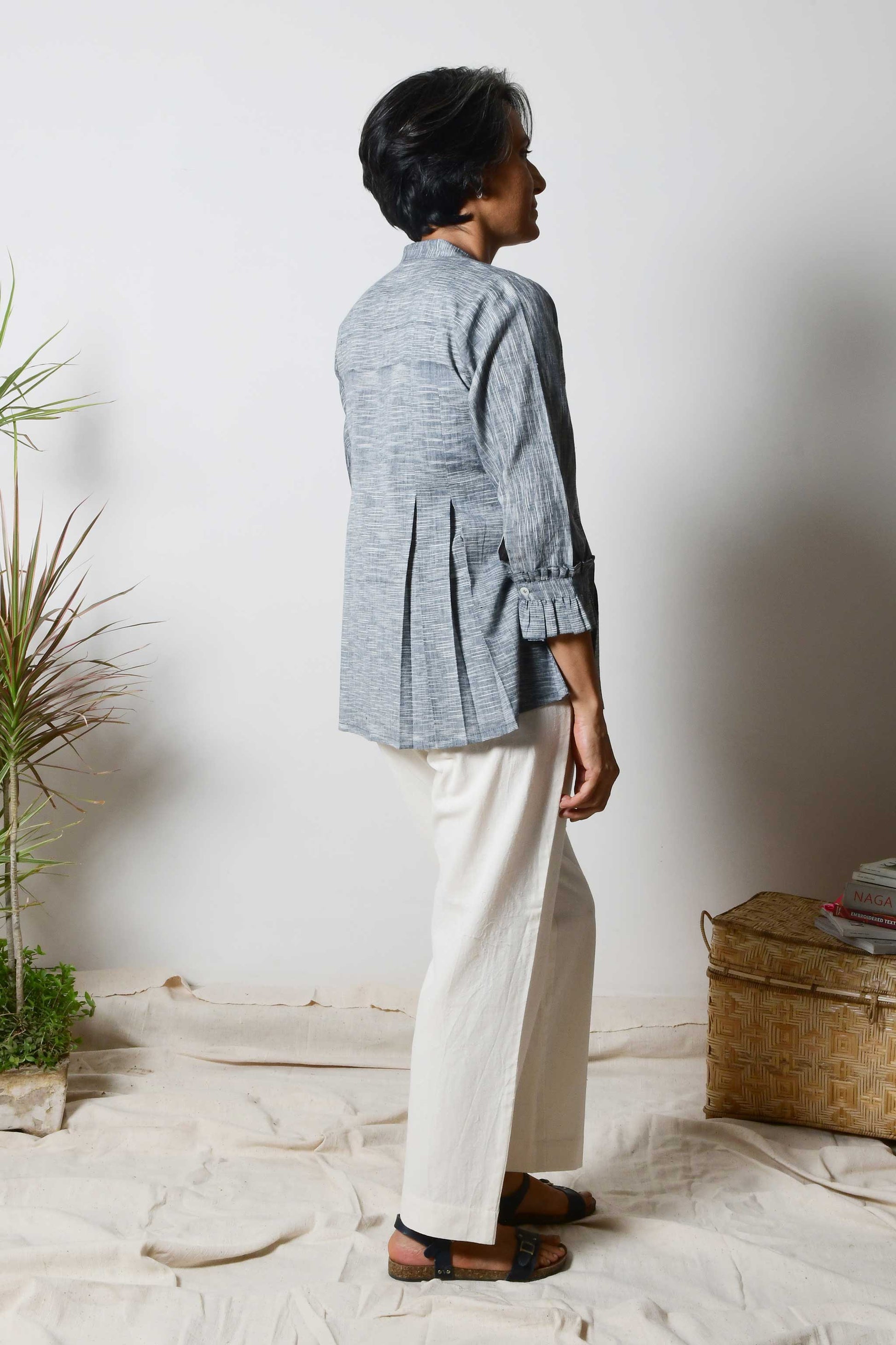 back pose of a Smiling woman with beautiful short grey hair wearing offwhite cotton pants and black cotton shirt blouse with texture on the fabric and box pleats on the top.