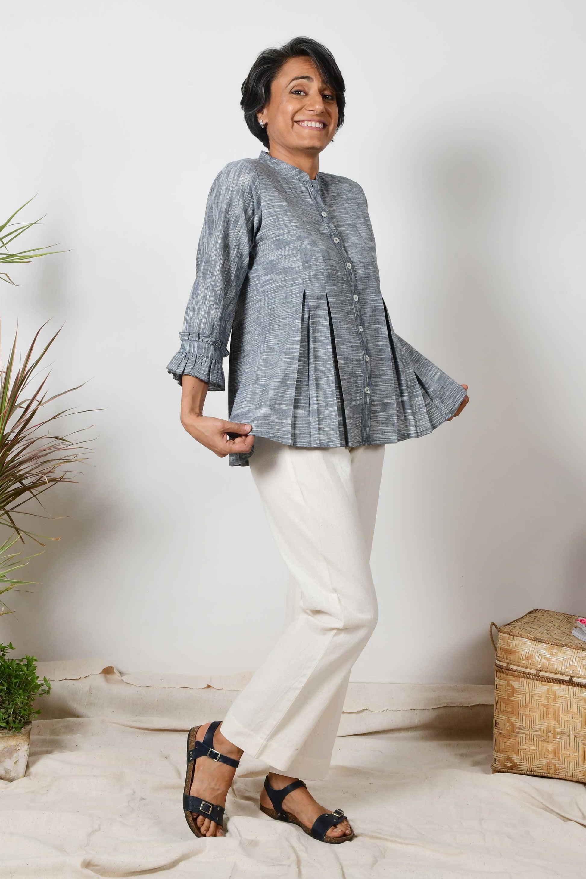 Smiling woman with beautiful short grey hair wearing offwhite cotton pants and black cotton shirt blouse with texture on the fabric and box pleats on the top.