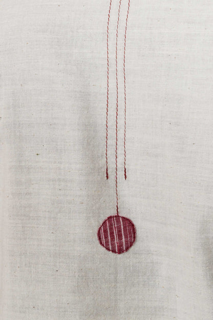 close up of stitching detail and a circular red patch on an off white cotton fabric base.