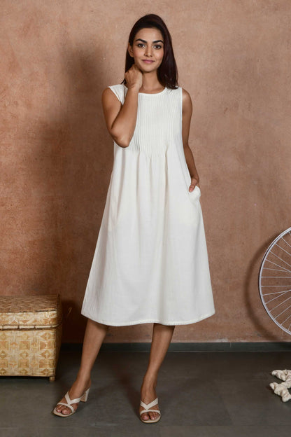 Front pose of a young indian model wearing an off white knee length a line dress with pleats till waist.