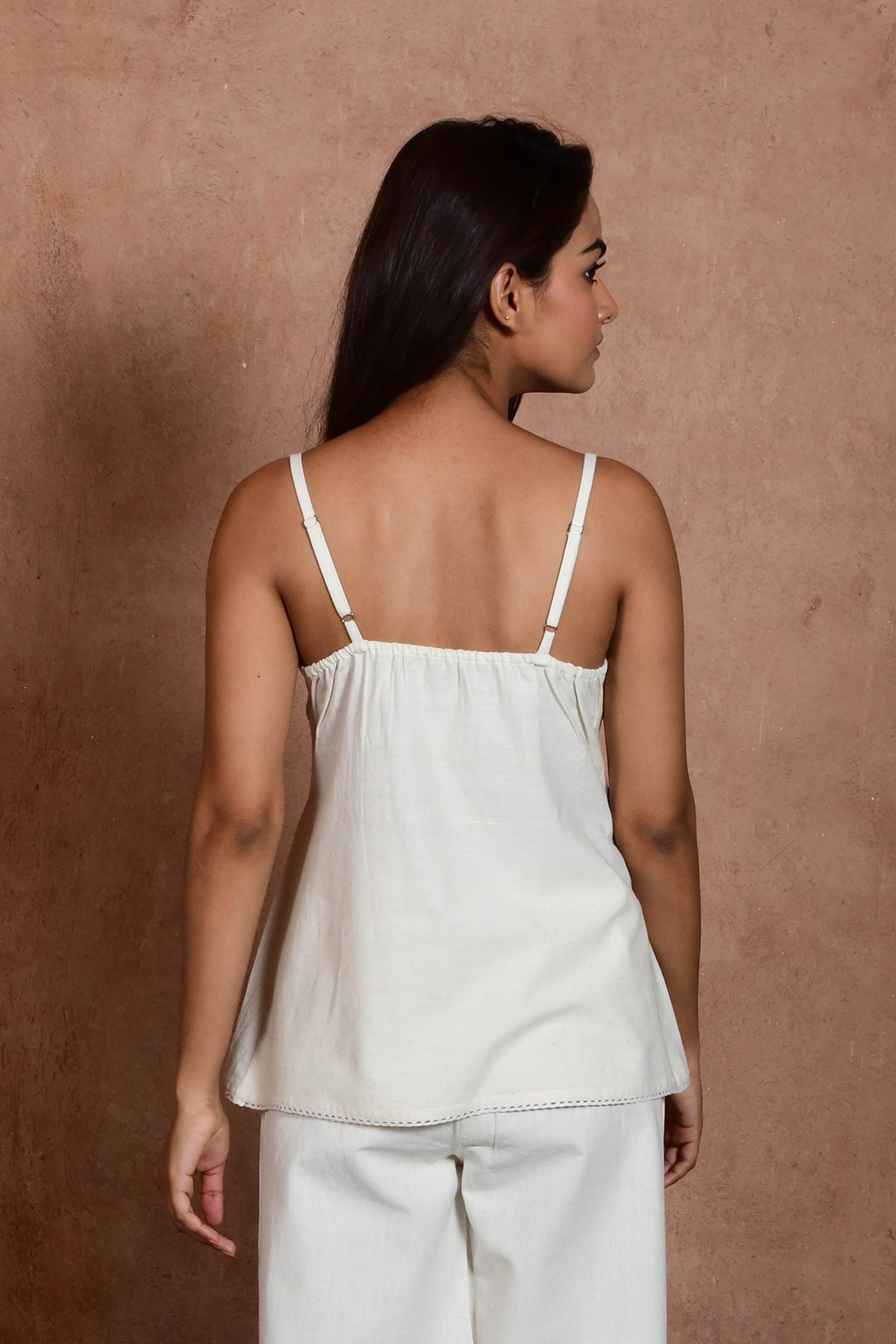 Back pose of an indian model wearing an off white spaghetti top with pin tucks.