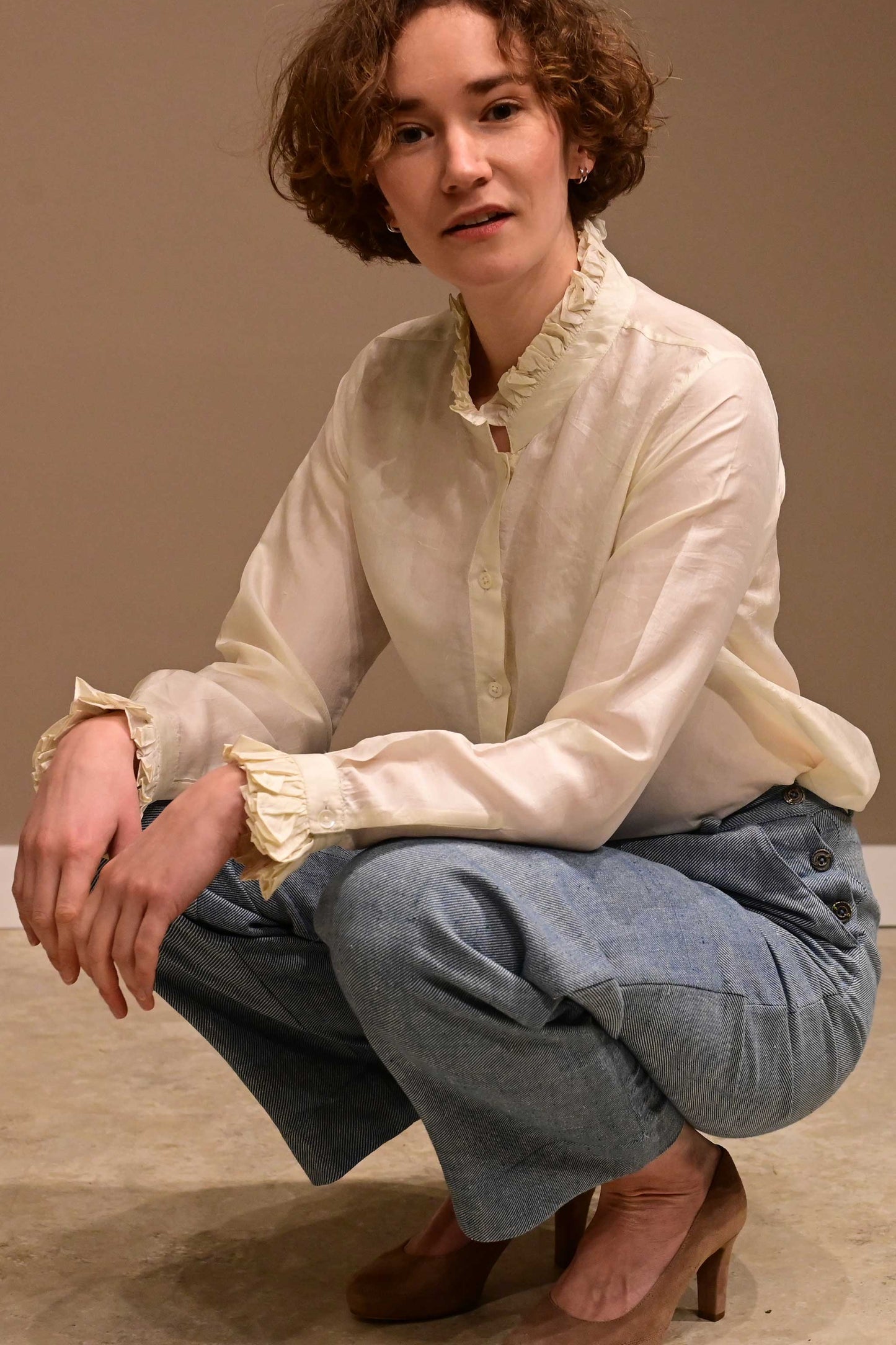 Close up of a sitting caucasian female model wearing white silk shirt and naturally dyed indian cotton denims.