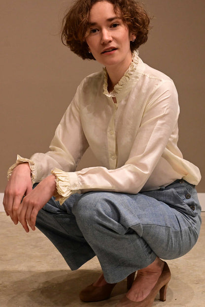 Close up of a sitting caucasian female model wearing white silk shirt and naturally dyed indian cotton denims.