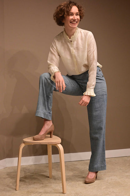 A smiling caucasian female model wearing hand reeled and hand spun invory white silk shirt and naturally dyed indigo denim pants that is made of indigenous cotton.