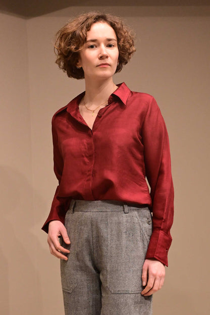 Front profile of a caucasian female model wearing a collared silk shirt in wine red color that is made from ethically sourced hand reeled and hand spun Indian silk.