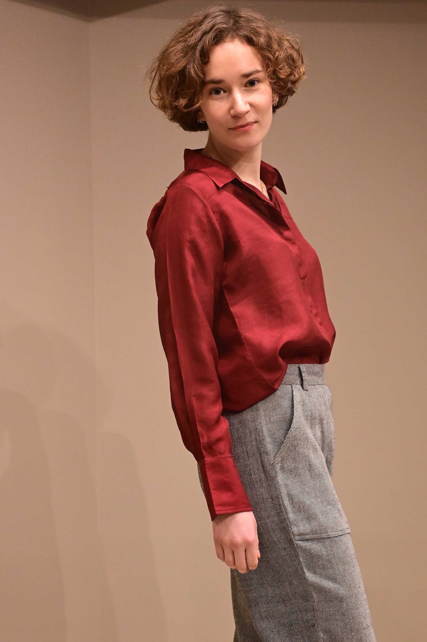 Side profile of a caucasian female model wearing a collared silk shirt in wine red color that is made from ethically sourced hand reeled and hand spun Indian silk.v