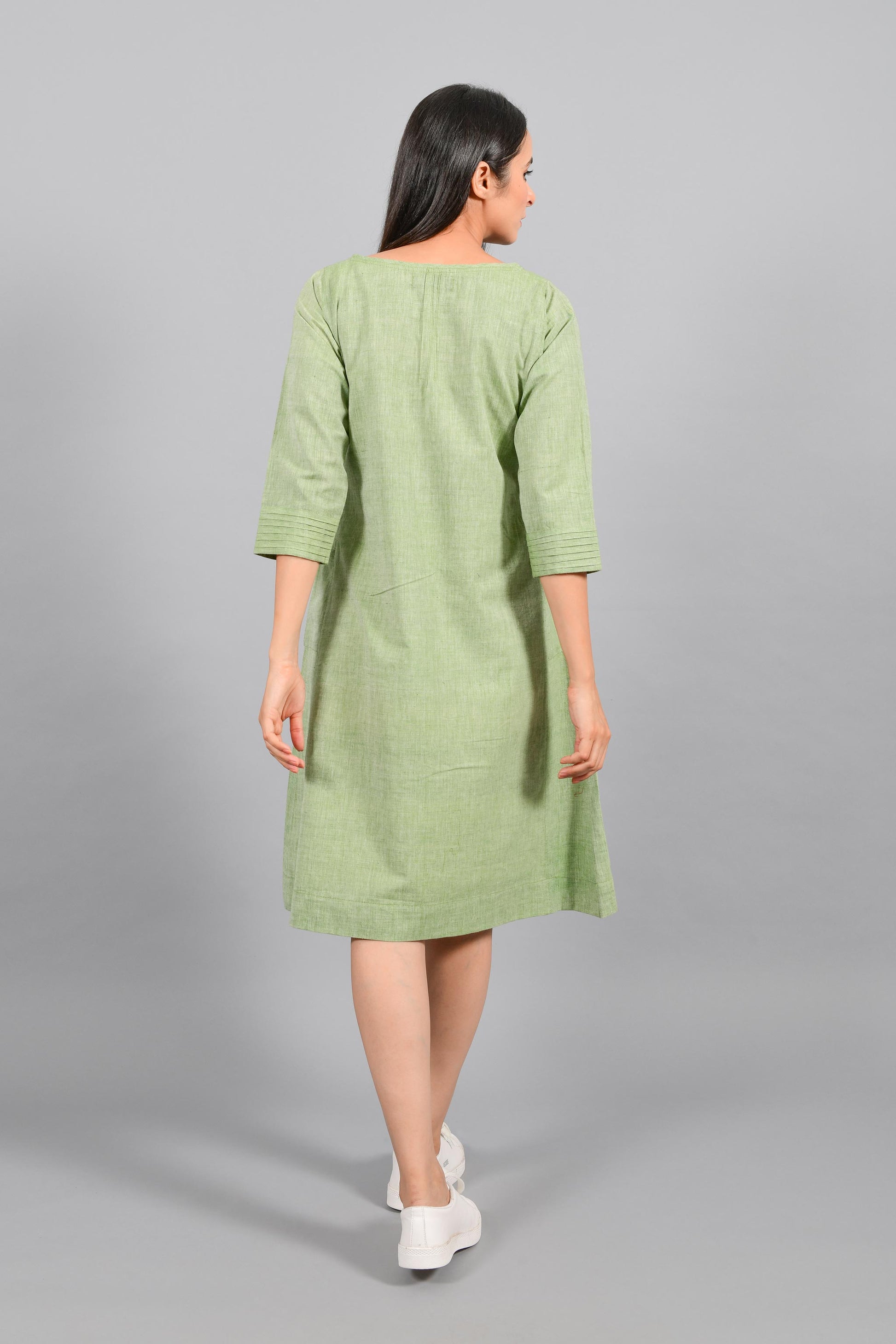 Back pose of an Indian female womenswear fashion model in a olive green chambray handspun and handwoven khadi cotton dress-kurta with pintucks on front by Cotton Rack.