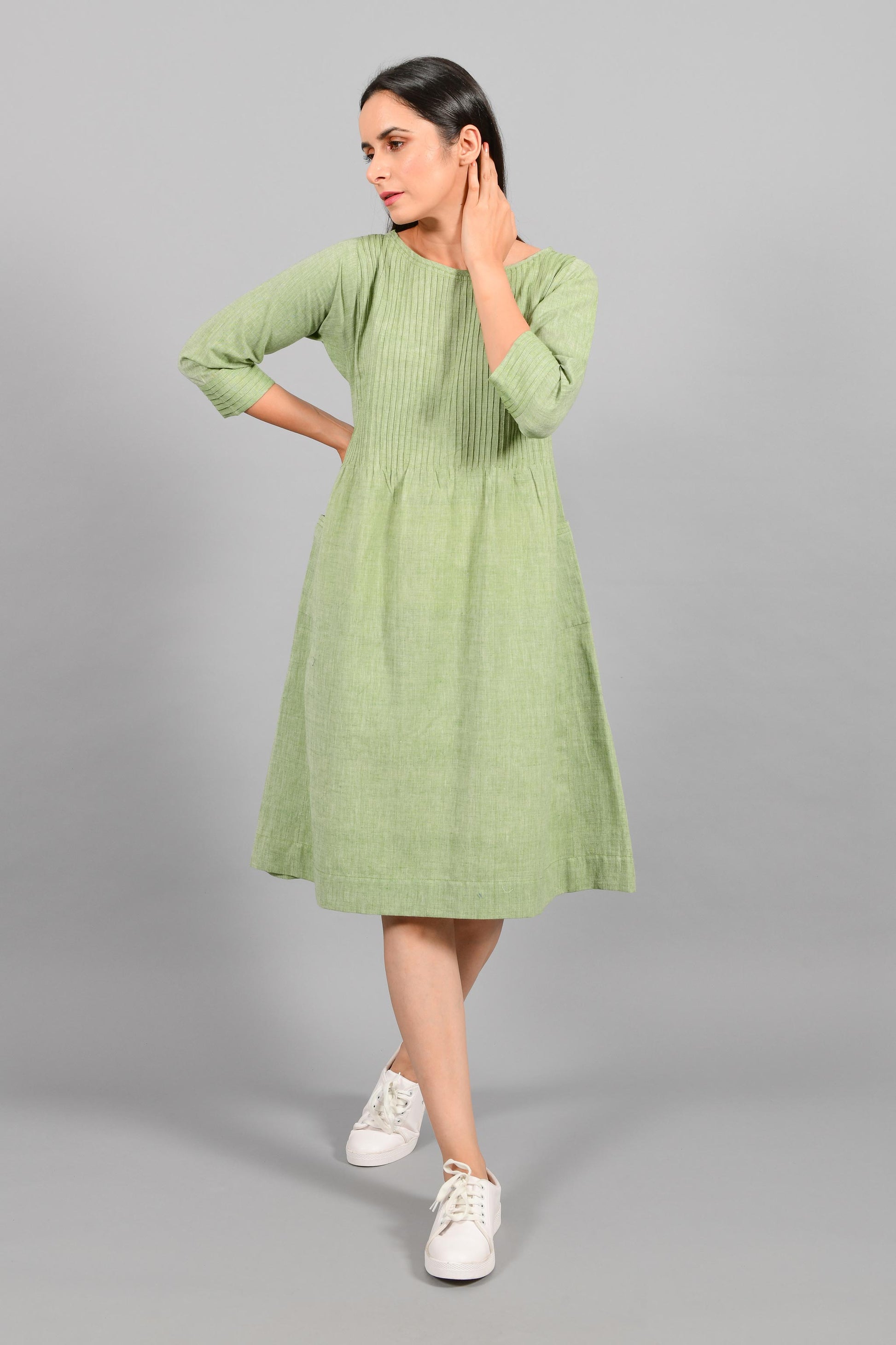 Front stylised pose of an Indian female womenswear fashion model in a olive green chambray handspun and handwoven khadi cotton dress-kurta with pintucks on front by Cotton Rack.