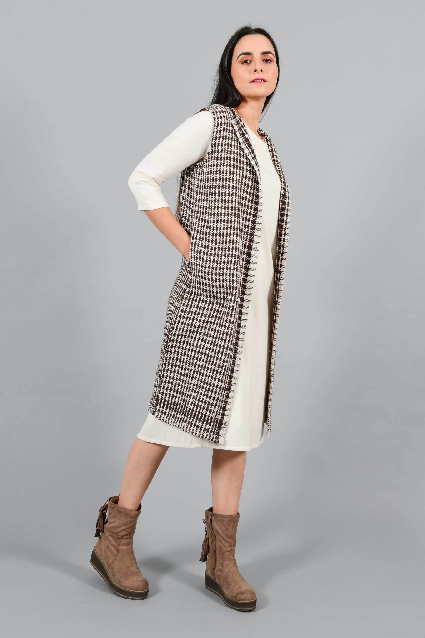 Side pose of an Indian Womenswear female model wearing Kora Brown handspun and handwoven khadi long Jacket over an off-white cashmere cotton dress by Cotton Rack.