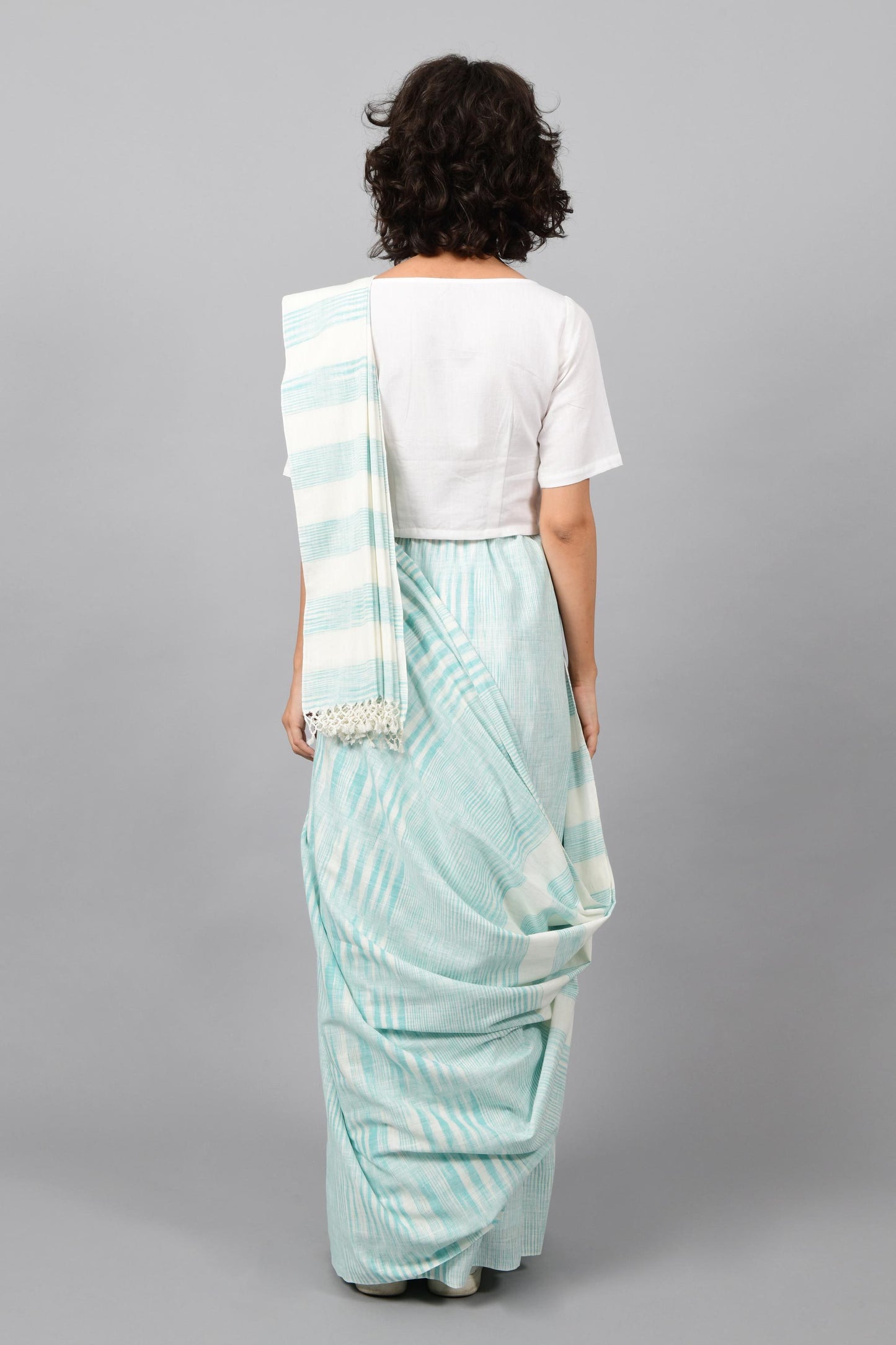 Back pose of a female womenswear fashion model draped in a aquamarine blue & white space dyed homespun and handwoven cotton sari by Cotton Rack.