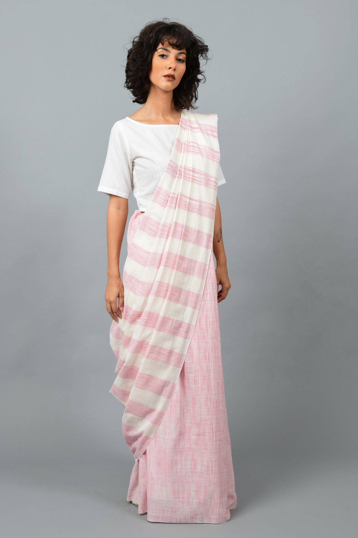 Side pose of a female womenswear fashion model draped in a pink & white space dyed homespun and handwoven cotton saree by Cotton Rack.