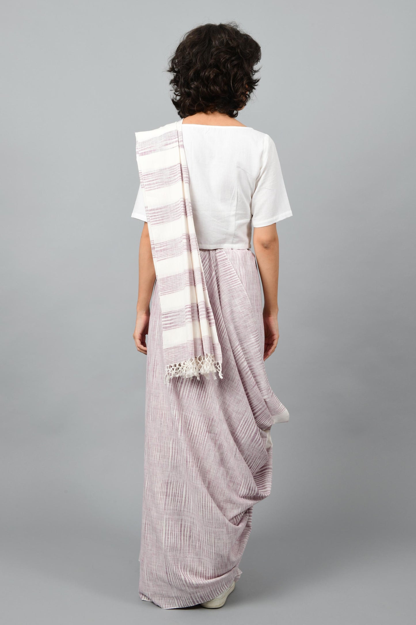 Back pose of a female womenswear fashion model draped in a purple & white space dyed homespun and handwoven cotton saree by Cotton Rack.