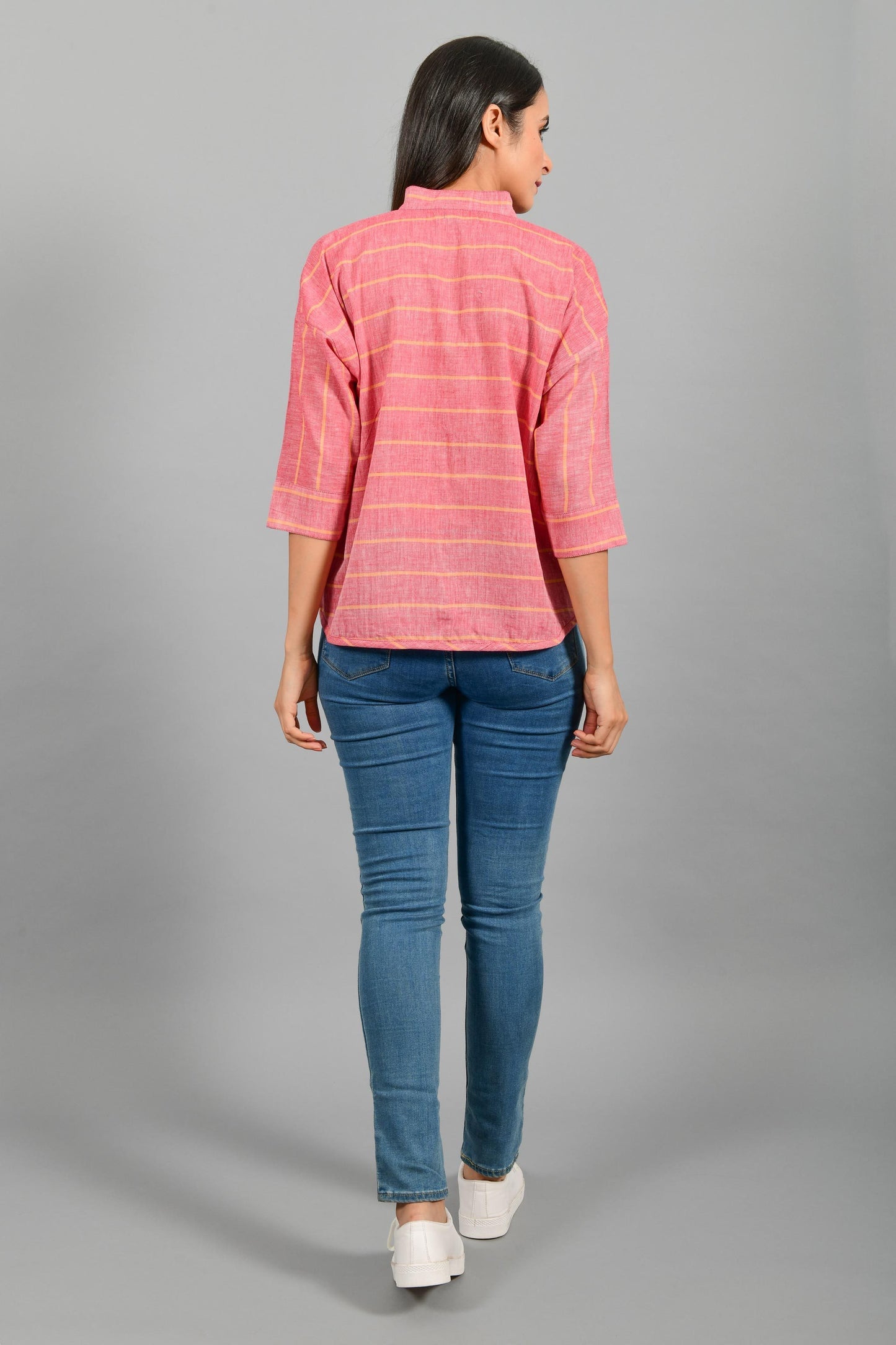Back pose of an Indian female womenswear fashion model in a red chambray with orange stripes handspun and handwoven khadi cotton free size top by Cotton Rack.