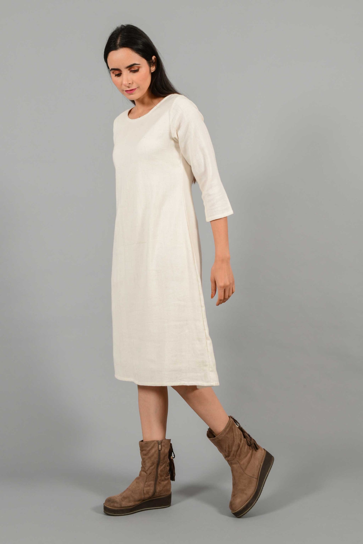 Side pose of an Indian female womenswear fashion model in an off-white Cashmere Cotton A-line Dress with box pleat on the back made using handspun and handwoven khadi cotton by Cotton Rack.