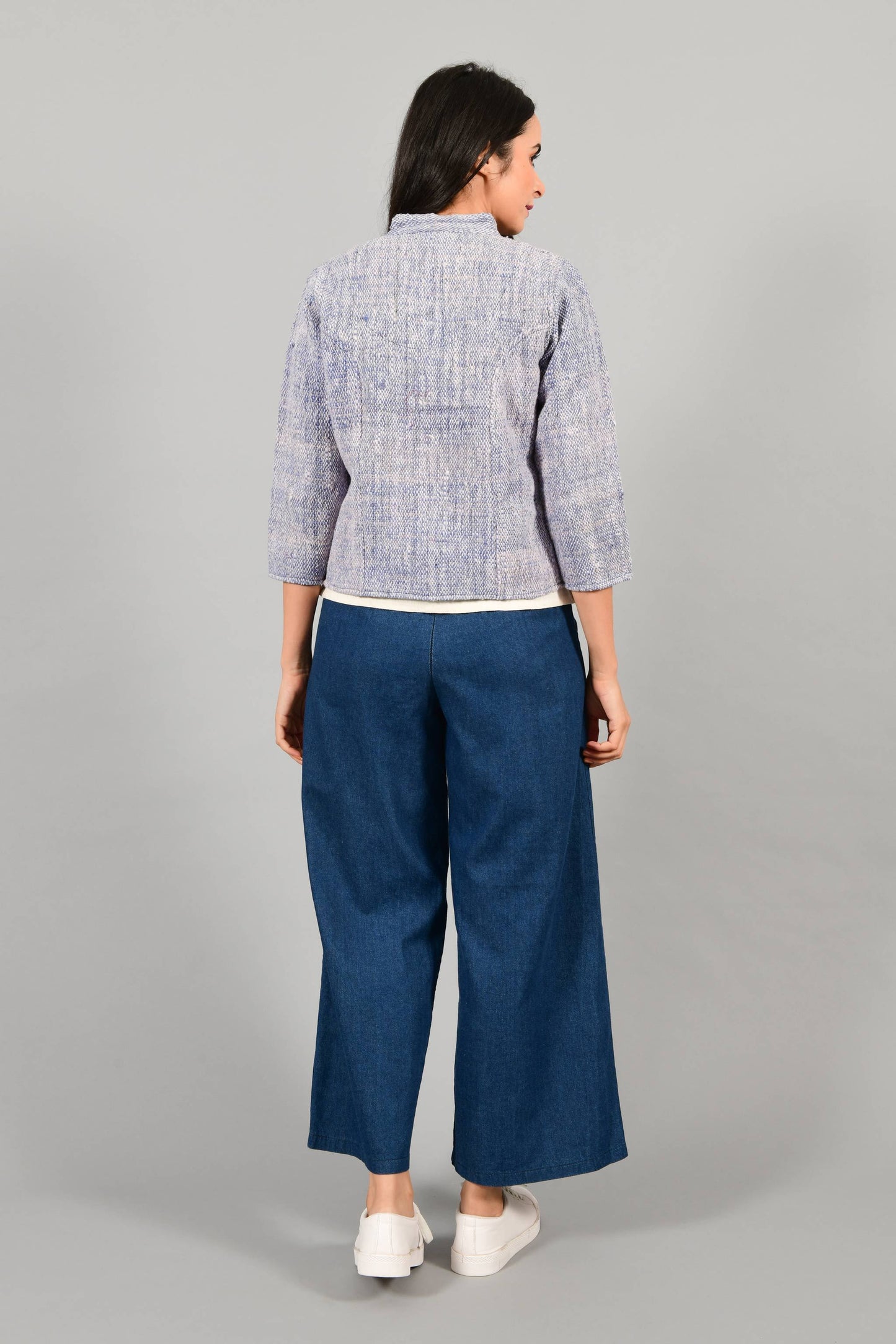 Back pose of an Indian Womenswear female model wearing Indigo Blue Gandhi Charkha spun and handwoven khadi buttoned mandarin collar Jacket over an off-white spaghetti and indigo palazzos by Cotton Rack.