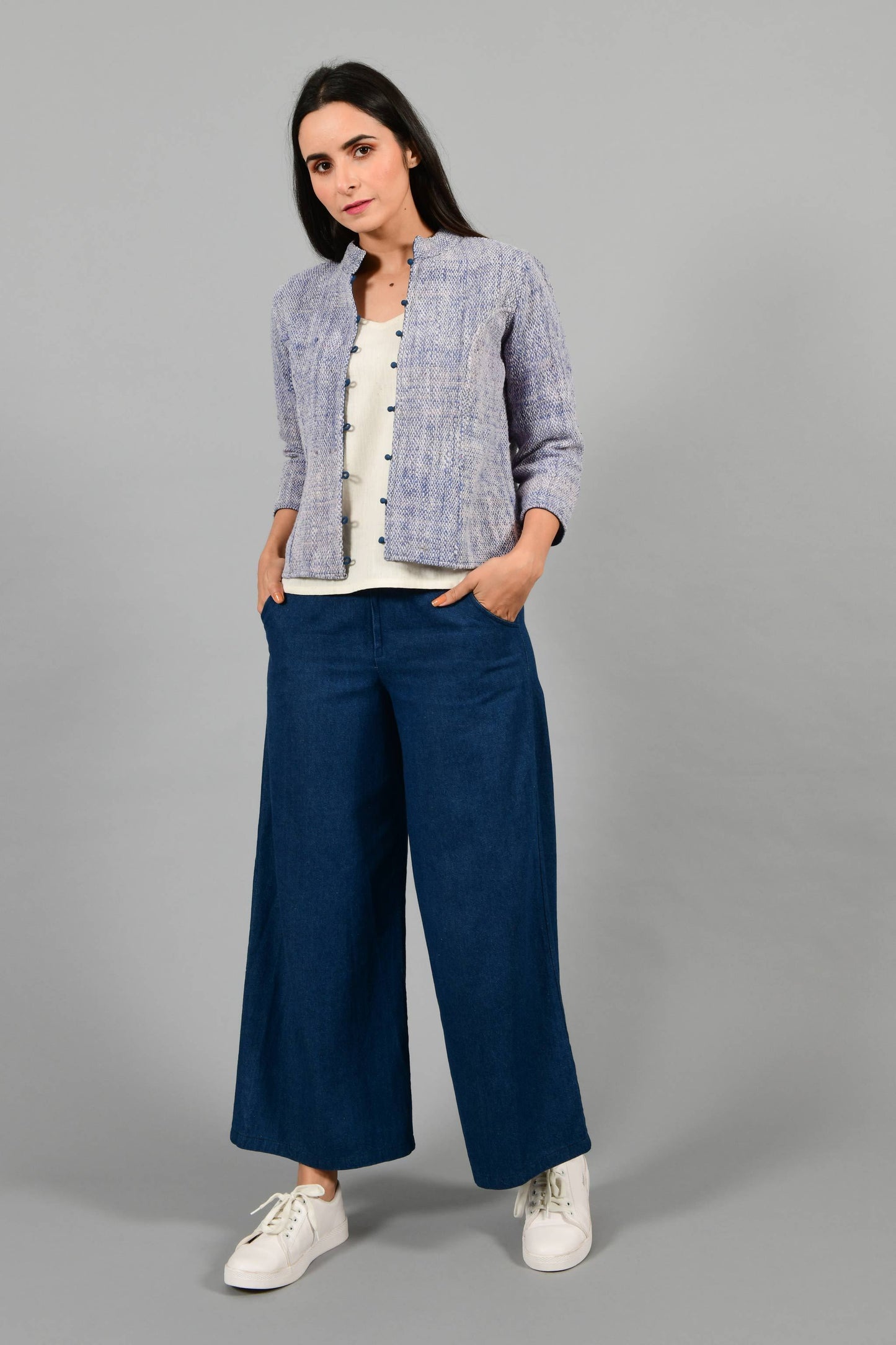 Front pose of an Indian Womenswear female model wearing Indigo Blue Gandhi Charkha spun and handwoven khadi buttoned mandarin collar Jacket over an off-white spaghetti and indigo palazzos by Cotton Rack.