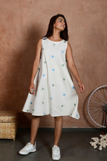 Creative front pose of an indian model wearing a handspun handloom cotton sleeveless dress that is knee length with green and blue polka dot patches.