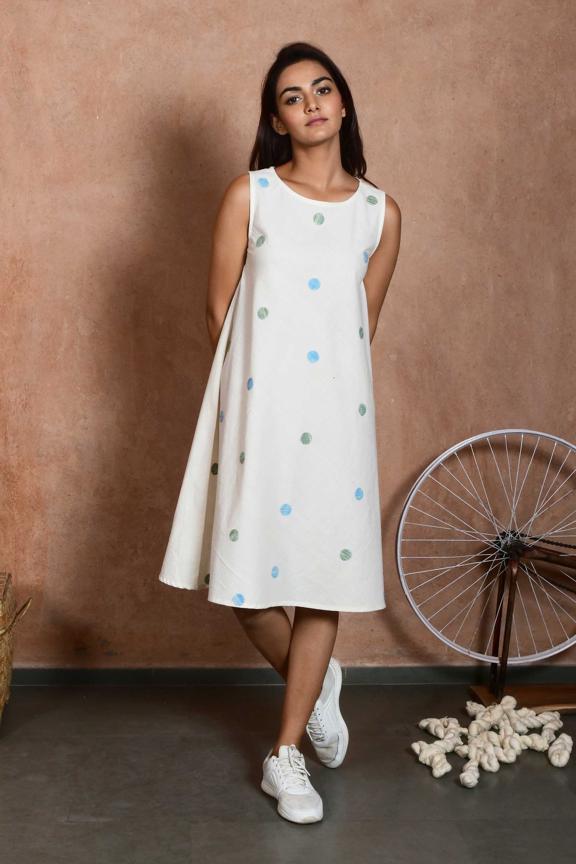 Front pose of an indian model wearing a handspun handloom cotton sleeveless dress that is knee length with green and blue polka dot patches.