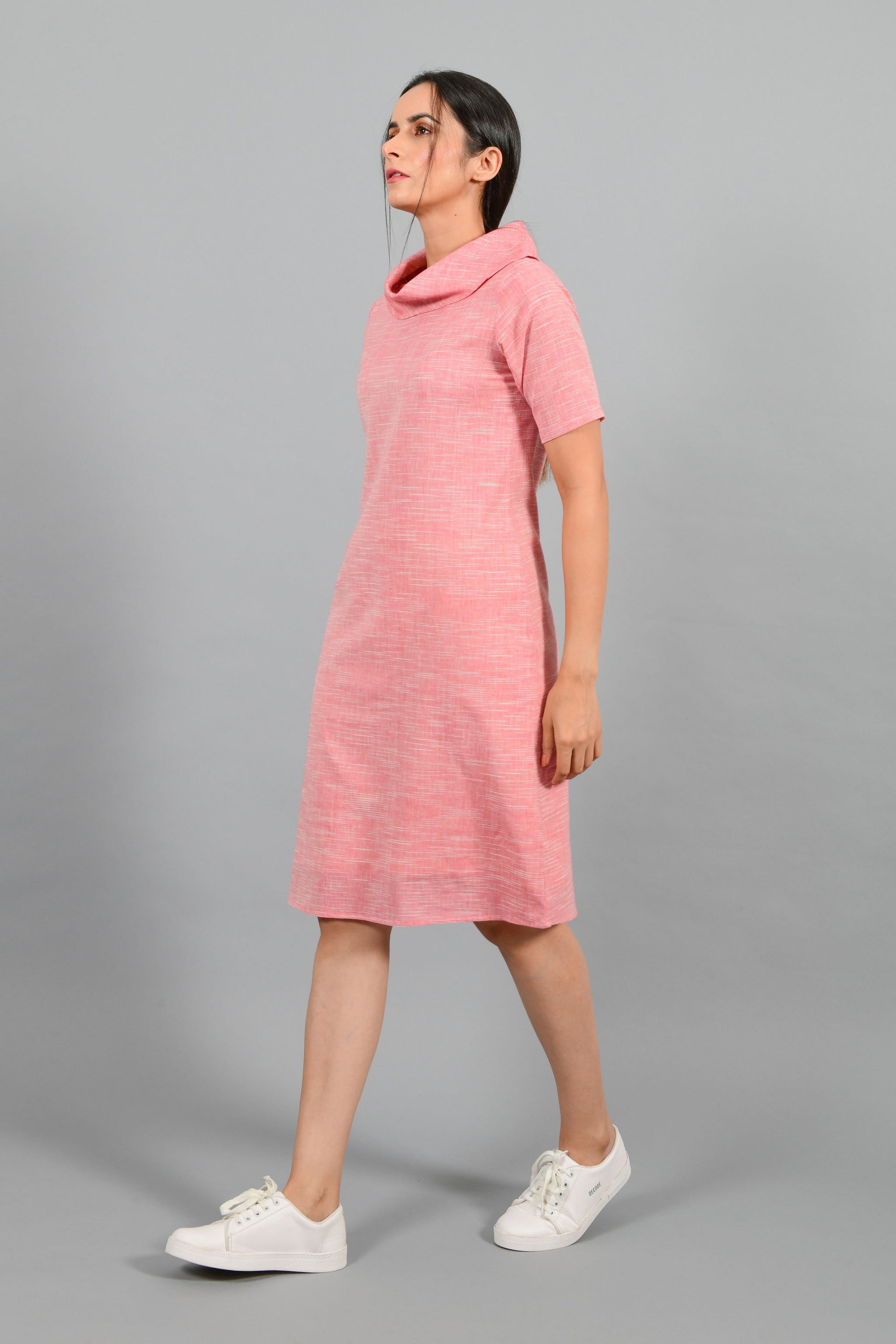 Side pose of an Indian female womenswear fashion model in a Pink and White space dyed cowl neck, elbow sleeve handspun and handwoven khadi cotton dress by Cotton Rack.
