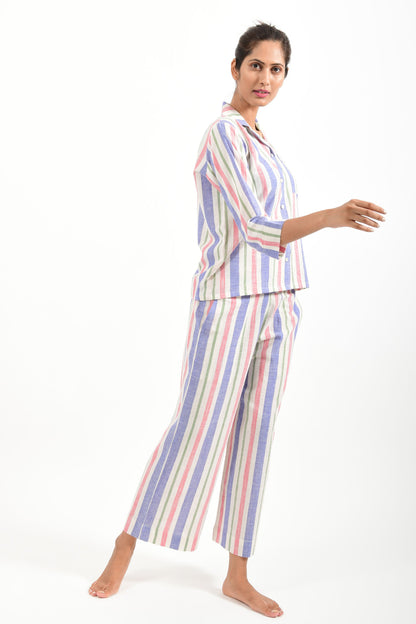 Side pose of an Indian female womenswear fashion model in a candy colored striped azo-free dyed handspun and handwoven khadi cotton nightwear pyjama & shirt by Cotton Rack.