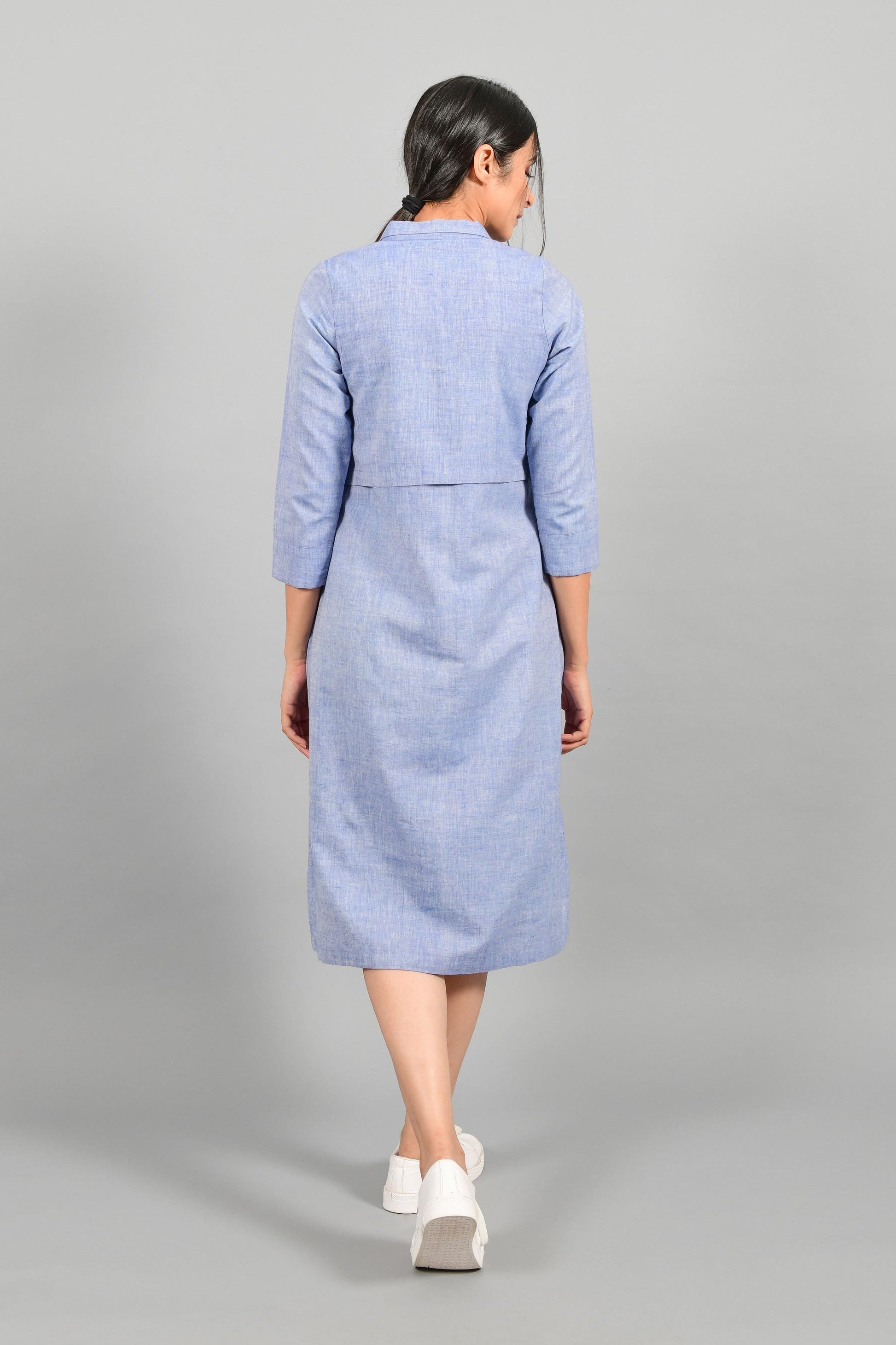 Back pose of an Indian female womenswear fashion model in a blue chambray handspun and handwoven khadi cotton shirt dress by Cotton Rack.