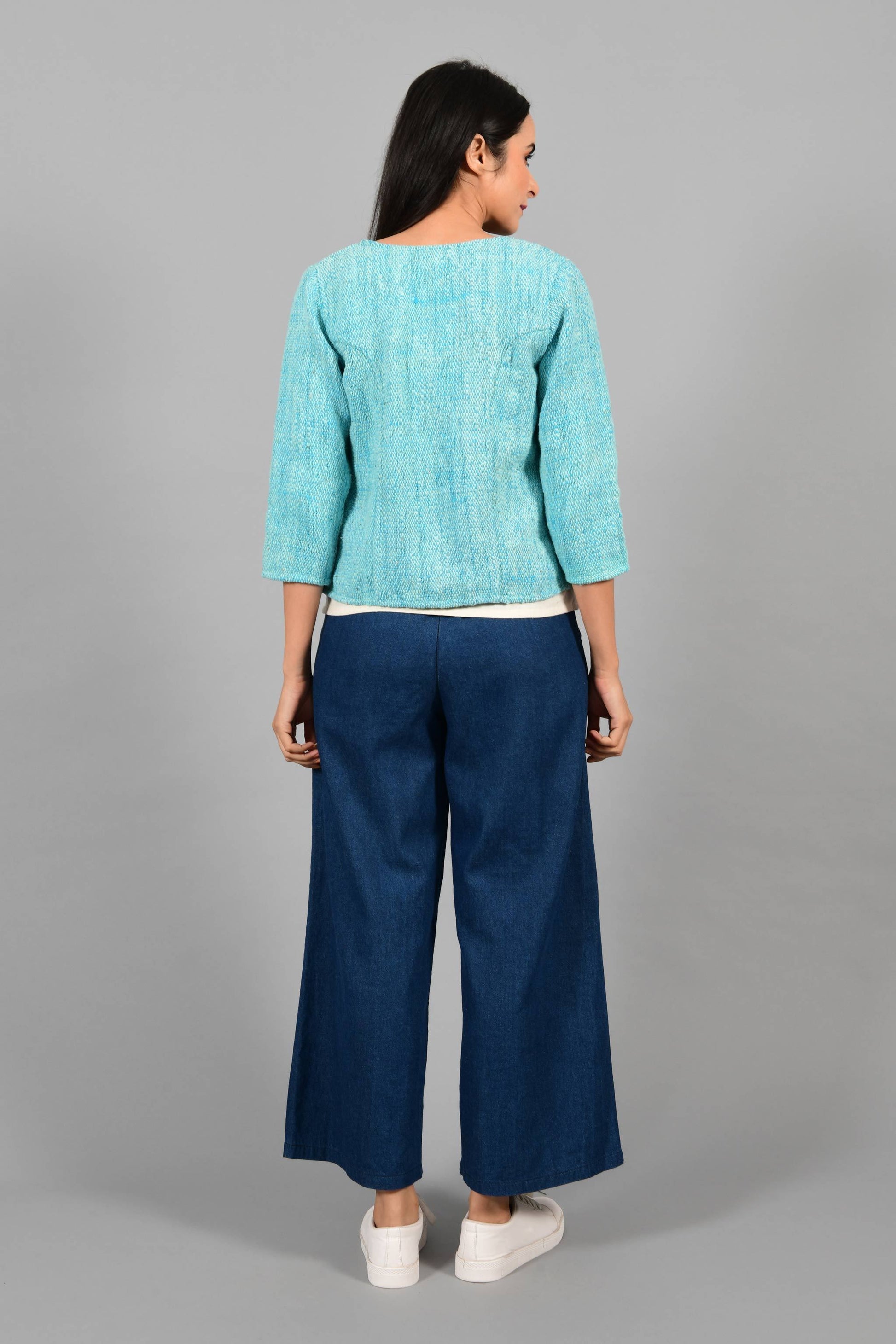 Back pose of an Indian Womenswear female model wearing aqua blue and Gandhi Charkha spun and handwoven khadi Jacket over an off-white spaghetti and indigo palazzos by Cotton Rack.