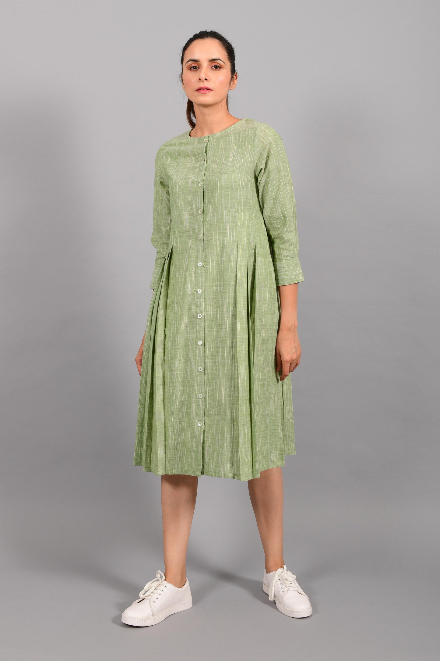 Front pose of an Indian female womenswear fashion model in a space dyed olive green handspun and handwoven khadi cotton pleated dress-kurta by Cotton Rack.