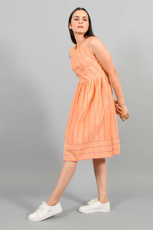 Stylised Side pose of an Indian female womenswear fashion model in a orange chambray handspun and handwoven khadi cotton with red stripes by Cotton Rack. The dress has gathers at waist. and the stripes are arranged in attractive manner.