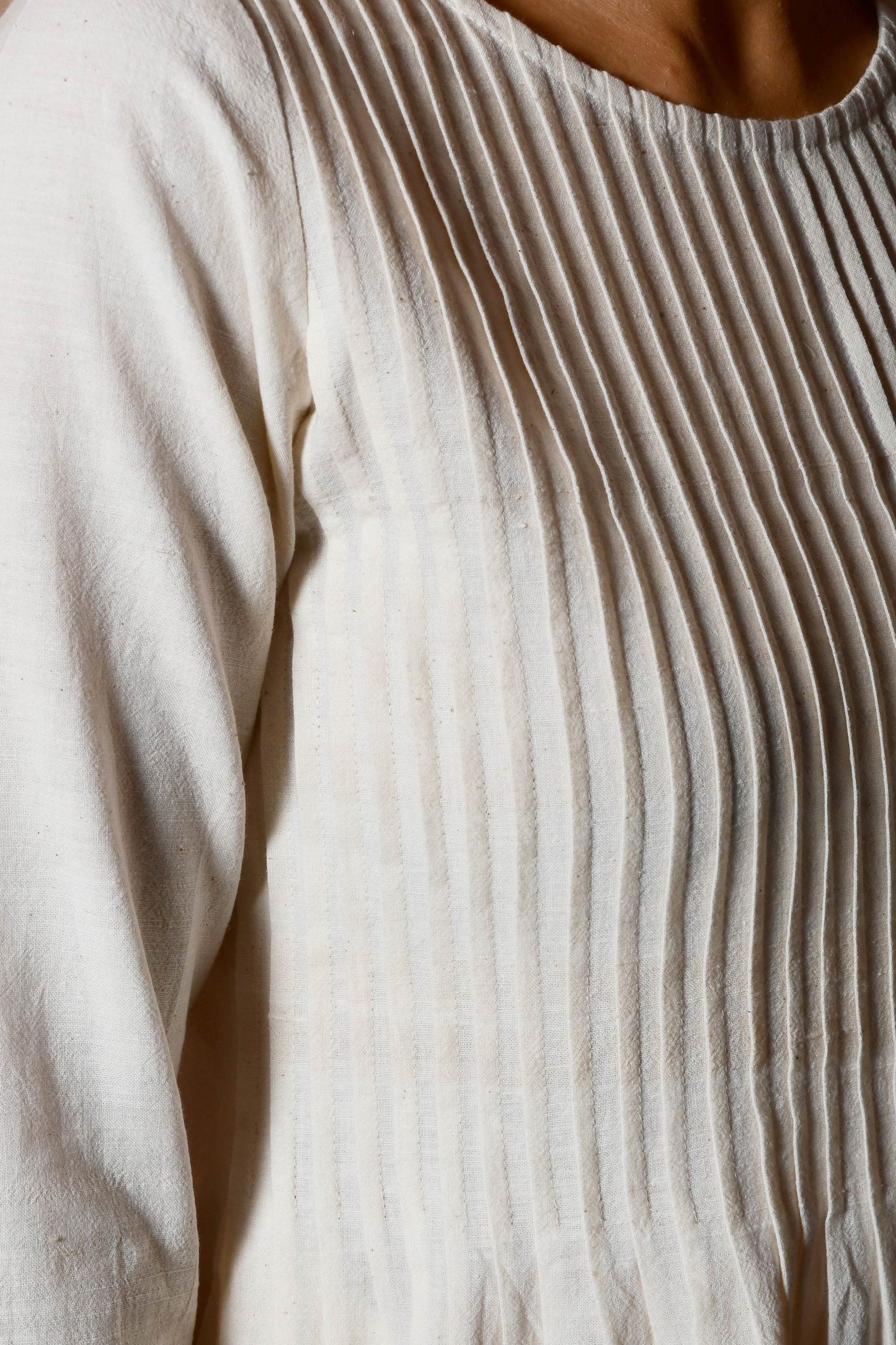 Close up of the knife pleats on the front of an off white dress.