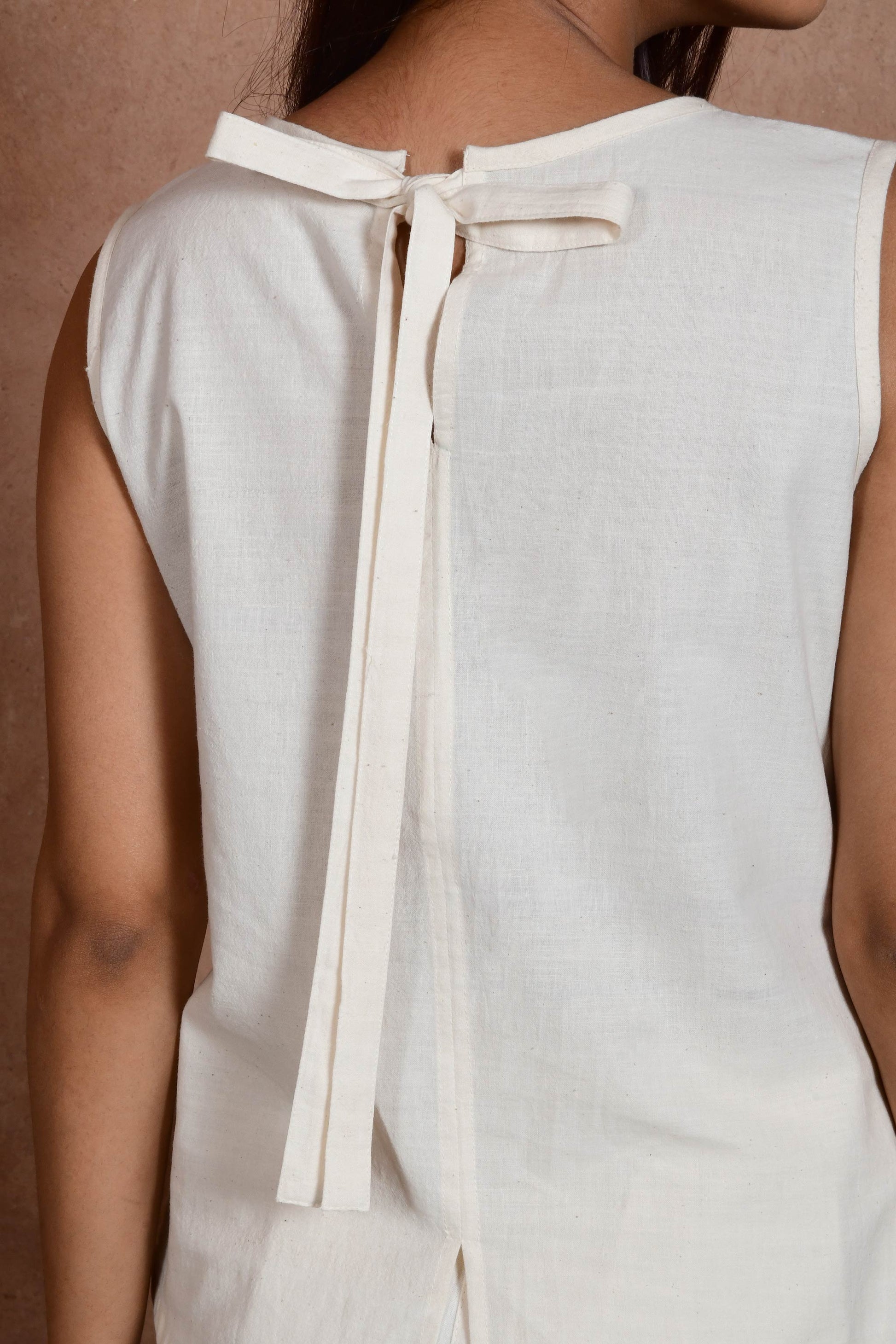 A close up of young Indian model posing wearing off white sleeveless top with a bow tied at the neck.