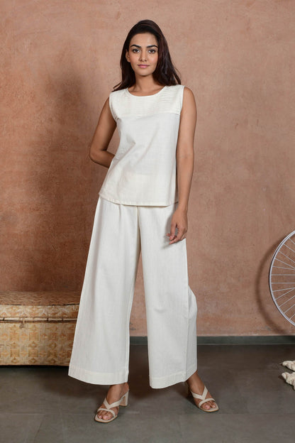 A front of young Indian model posing wearing off white sleeveless pleated top and straight pants.