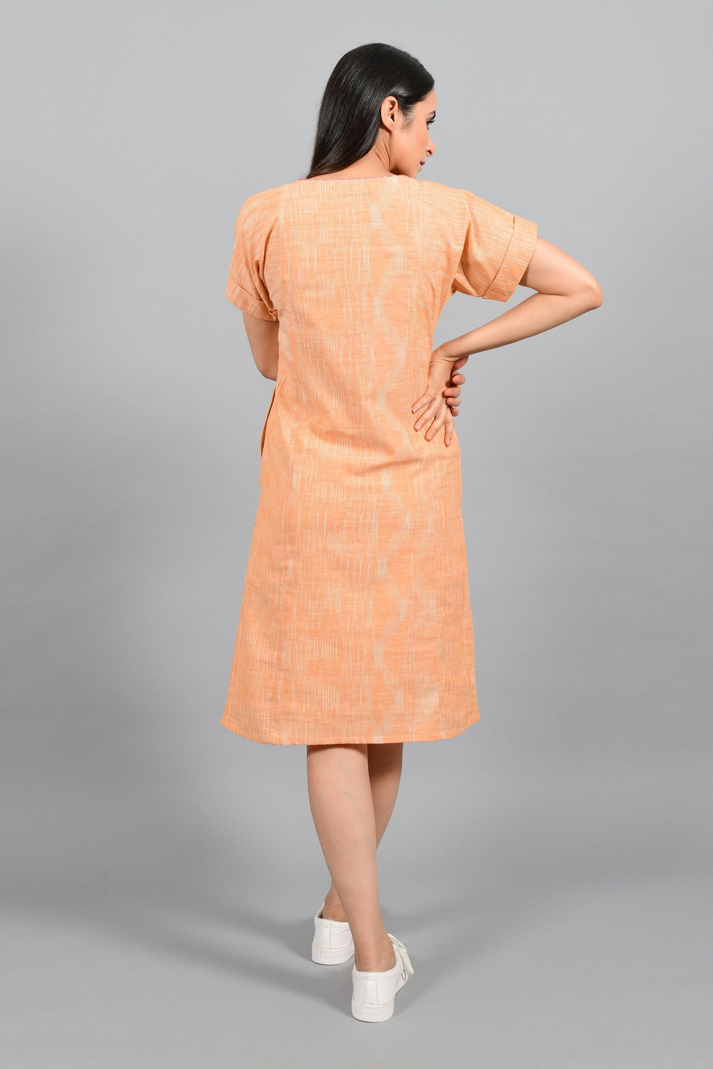 Back pose of an Indian female womenswear fashion model in an orange space dyed handspun and handwoven khadi cotton panelled dress by Cotton Rack.