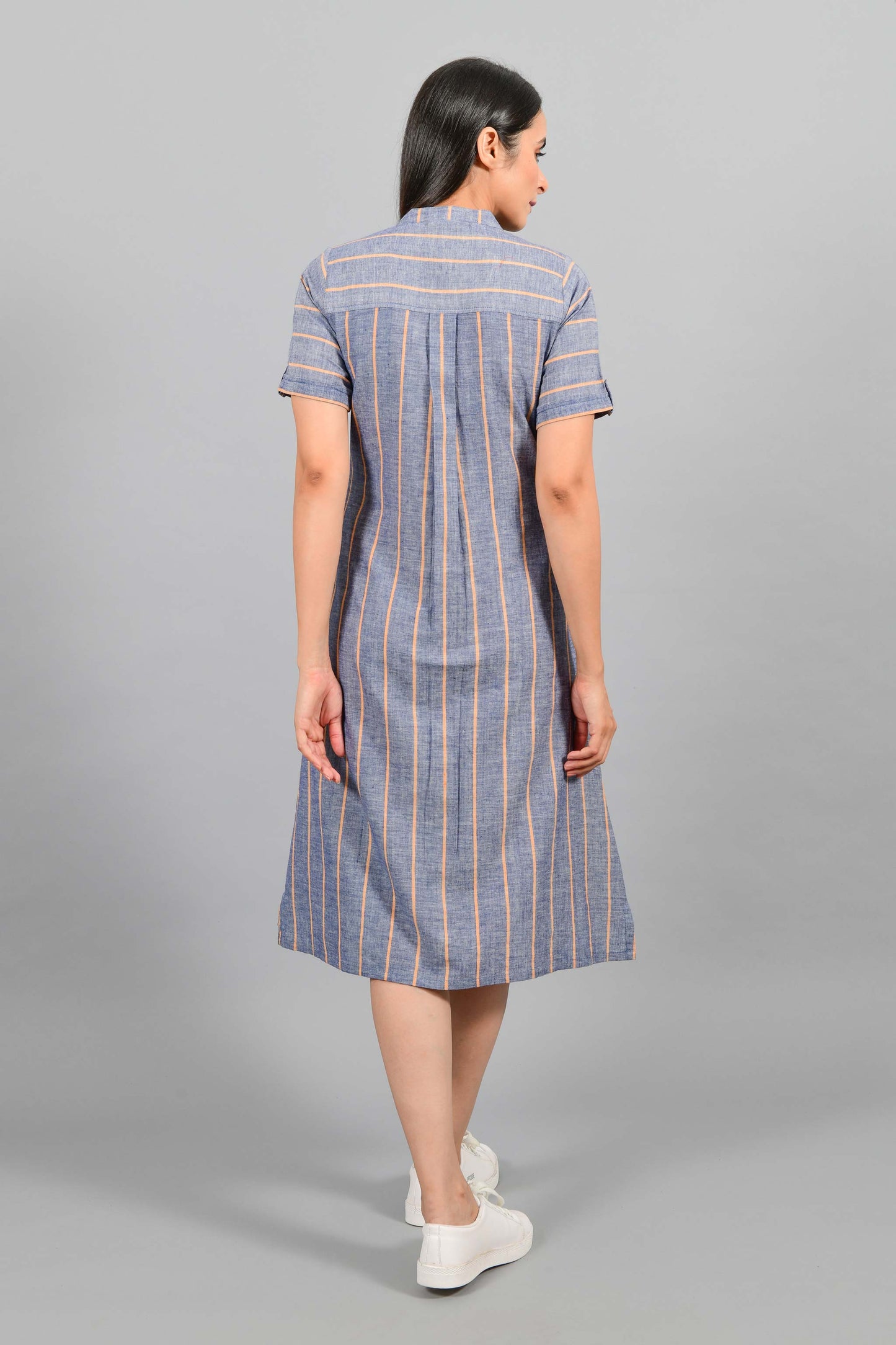 Back pose of an Indian female womenswear fashion model in a Blue chambray with orange stripes handspun and handwoven khadi cotton dress-kurta by Cotton Rack.