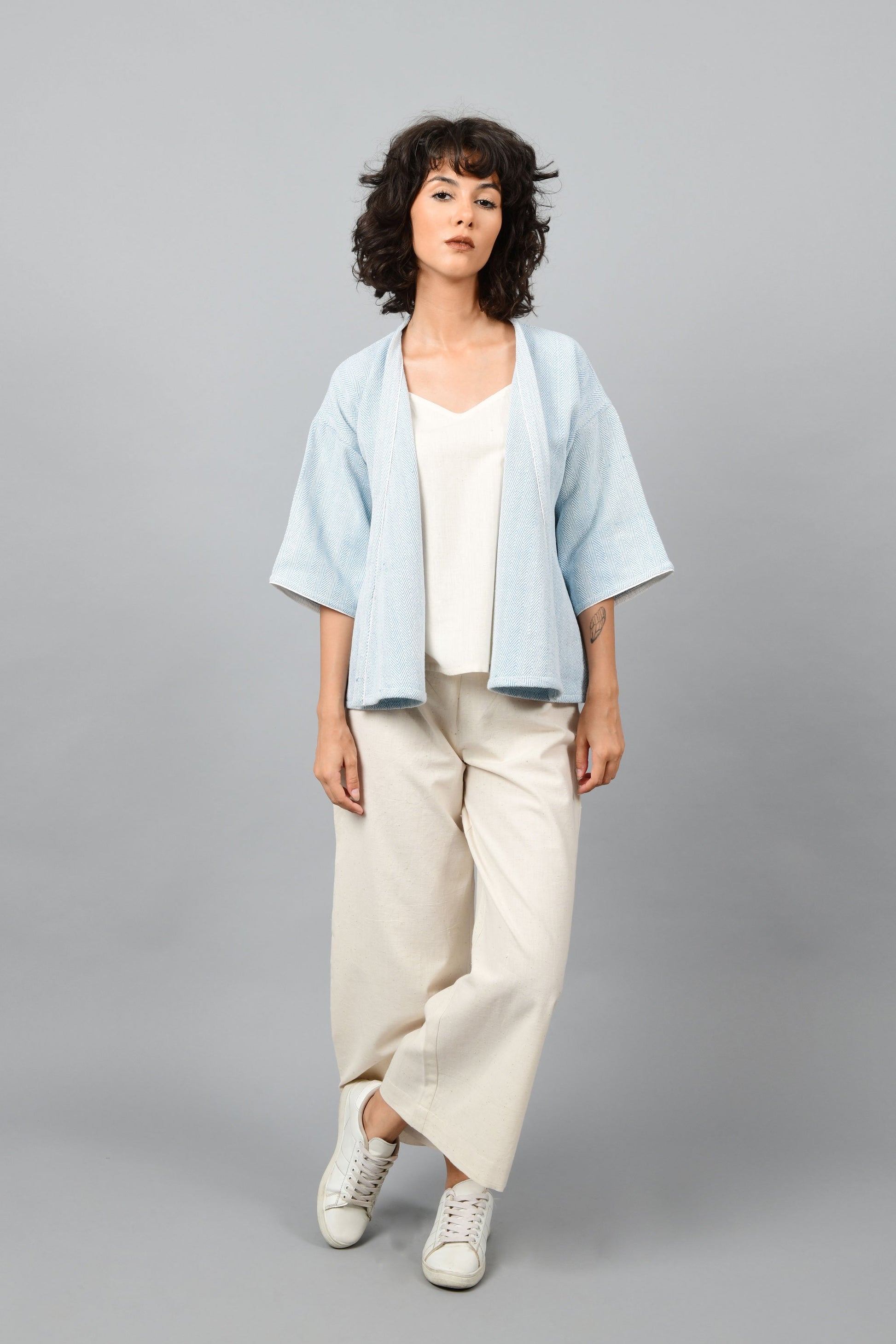 Model wearing anti-fit short blue shrug made in pointed twill with handspun and handwoven khadi cotton. Paired with off-white spaghetti, palazzos and white shoes.