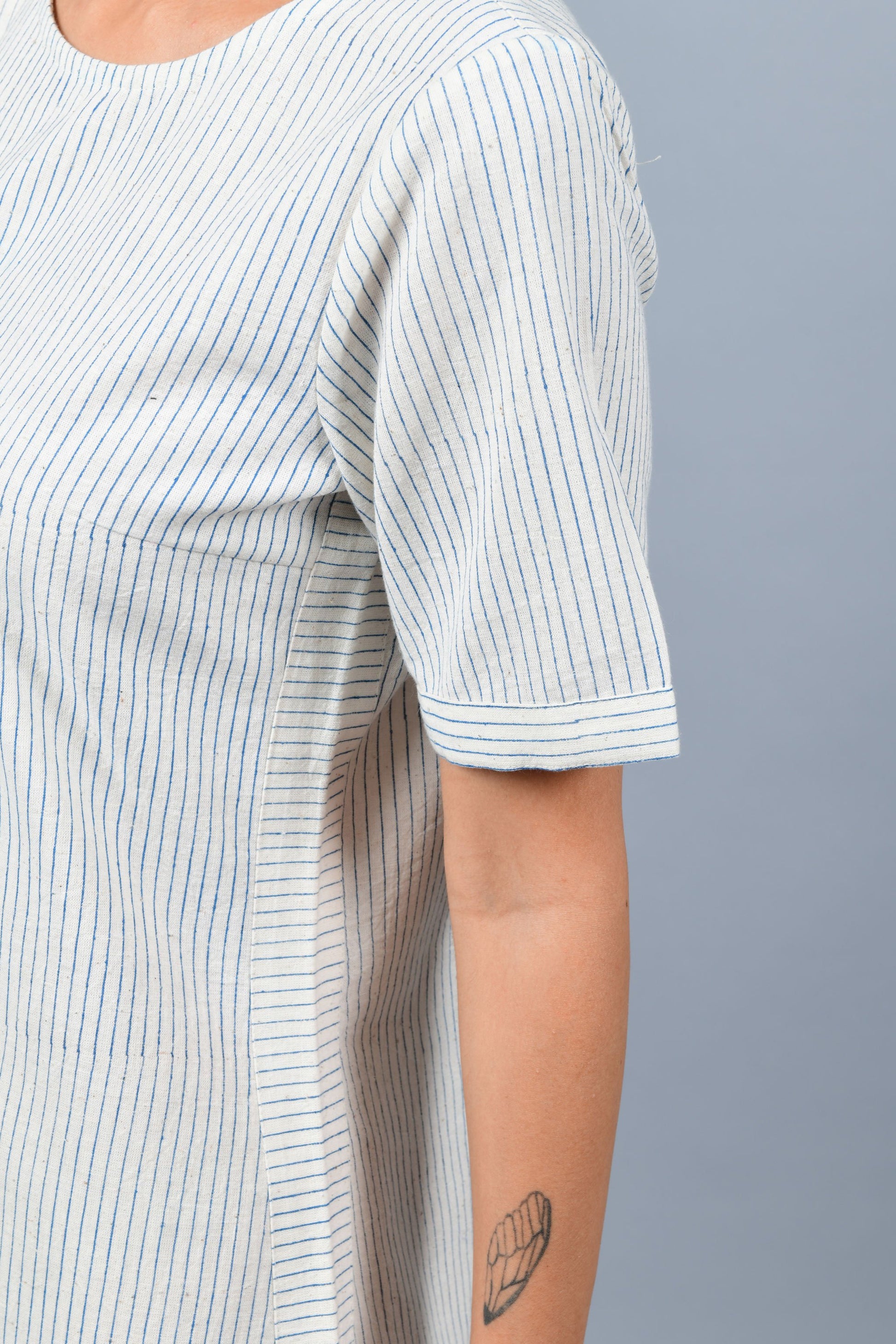 close-up of a womenswear fashion model wearing minimalistic a-line round bottom dress by Cotton Rack printed with blue stripes using brass block printing over handspun handwoven khadi cotton from maheshwar