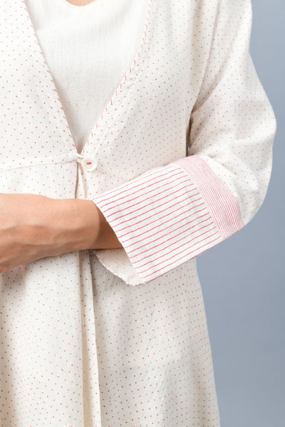 Close of a long flared off-white, natural khadi cotton shrug buttoned up in the front, hand block printed with fine red dots and red stripes on the sleeve hem.