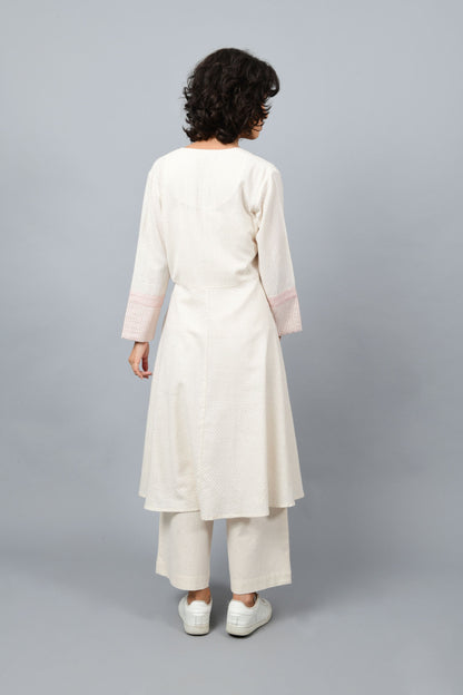 Back of the long flared off-white, natural khadi cotton shrug buttoned up, hand block printed with red dots and red stripes on the sleeve hem.