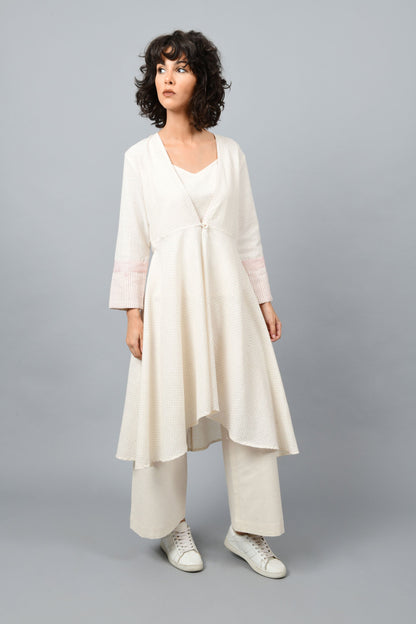 Model wearing a long flared off-white, natural khadi cotton shrug buttoned up in the front, hand block printed with red dots and red stripes on the sleeve hem.