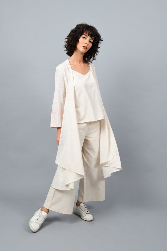 Model wearing a long flared off-white, natural khadi cotton shrug posing with quarter front and opened up in the front, hand block printed with red dots and red stripes on the sleeve hem.