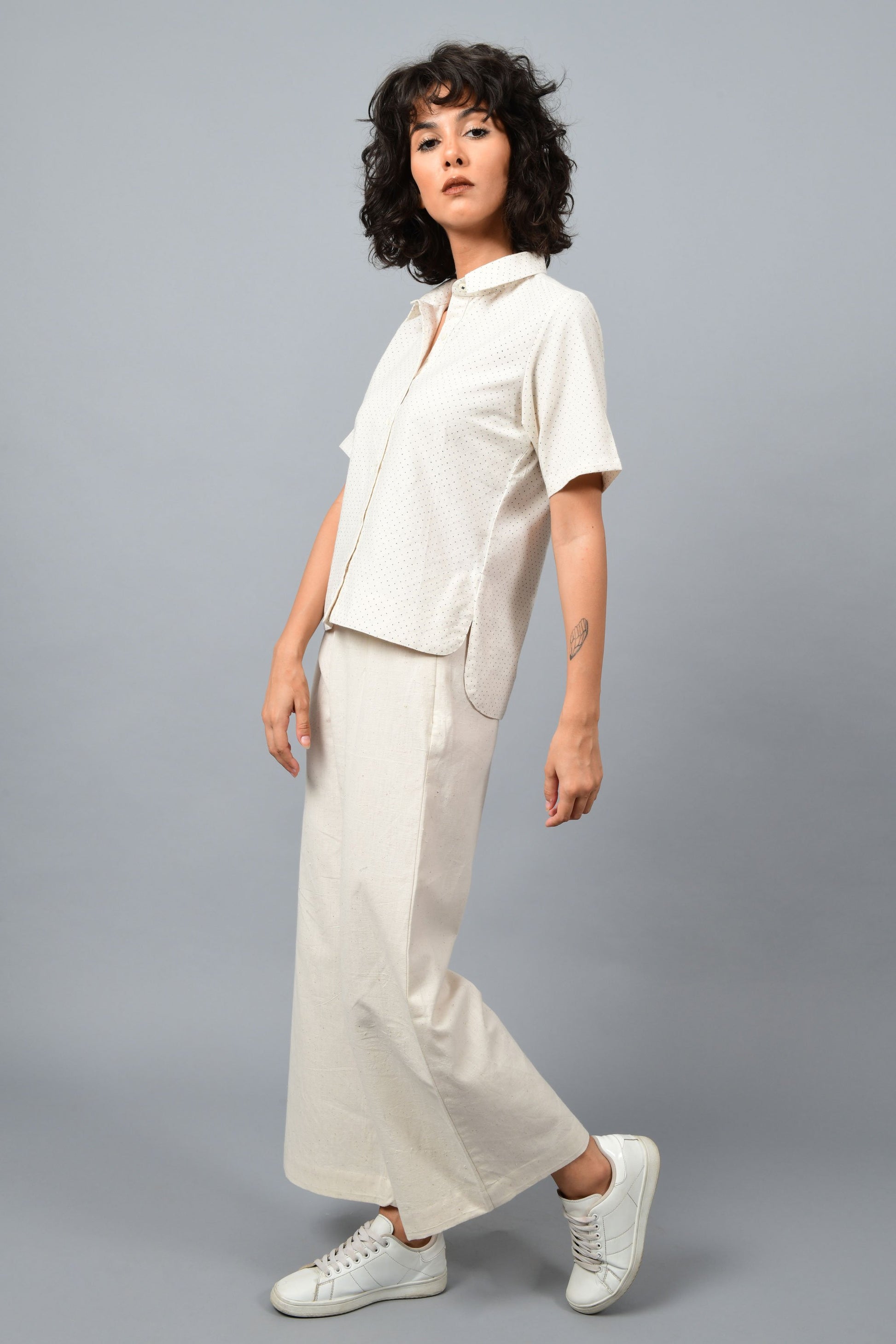 Model wearing off-white Khadi cotton relaxed shirt top printed with fine blue dots printed using metal block by Cotton Rack inspired by artist agnes martin. Posing facing left for the camera. 