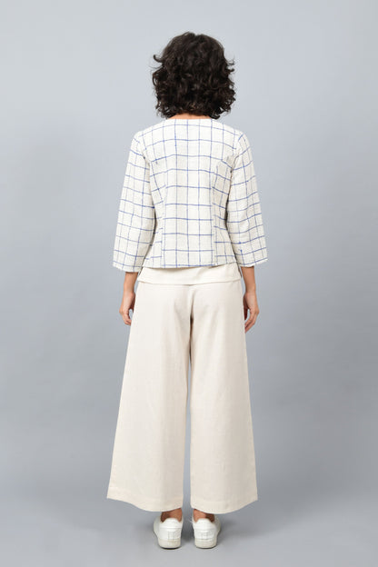 Model showing the back of open short jacket in thicker white handspun and handwoven khadi cotton with big blue checks over off-white spaghetti top and off-white palazzos paired with white sneakers.