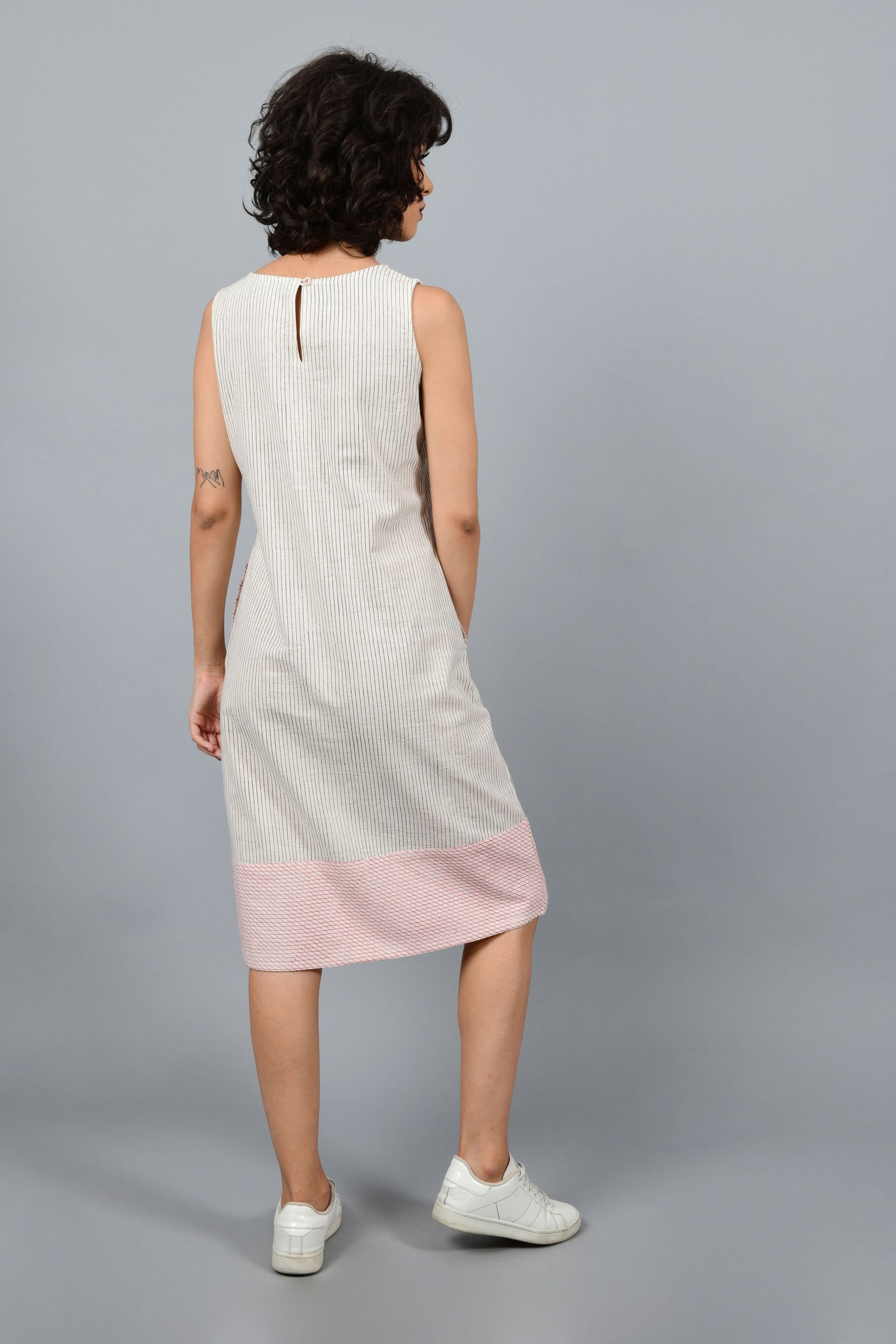 Model wearing black block printed black pin stripes with red checks on the hem on off-white handspun and handwoven khadi cotton sleeveless dress, showing the back.