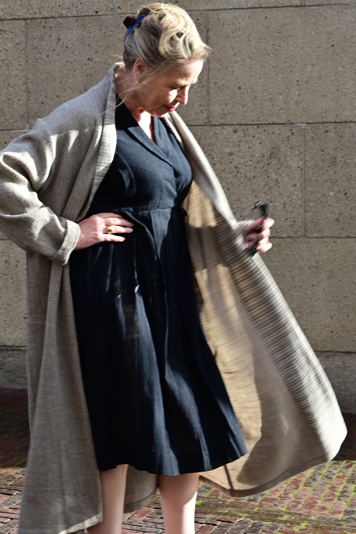 A middle aged european model posing wearing brown woolen long shrug with ivory woven pattern on the collar. This shrug is made of handspun and handwoven Indian sheep wool by Cotton Rack.