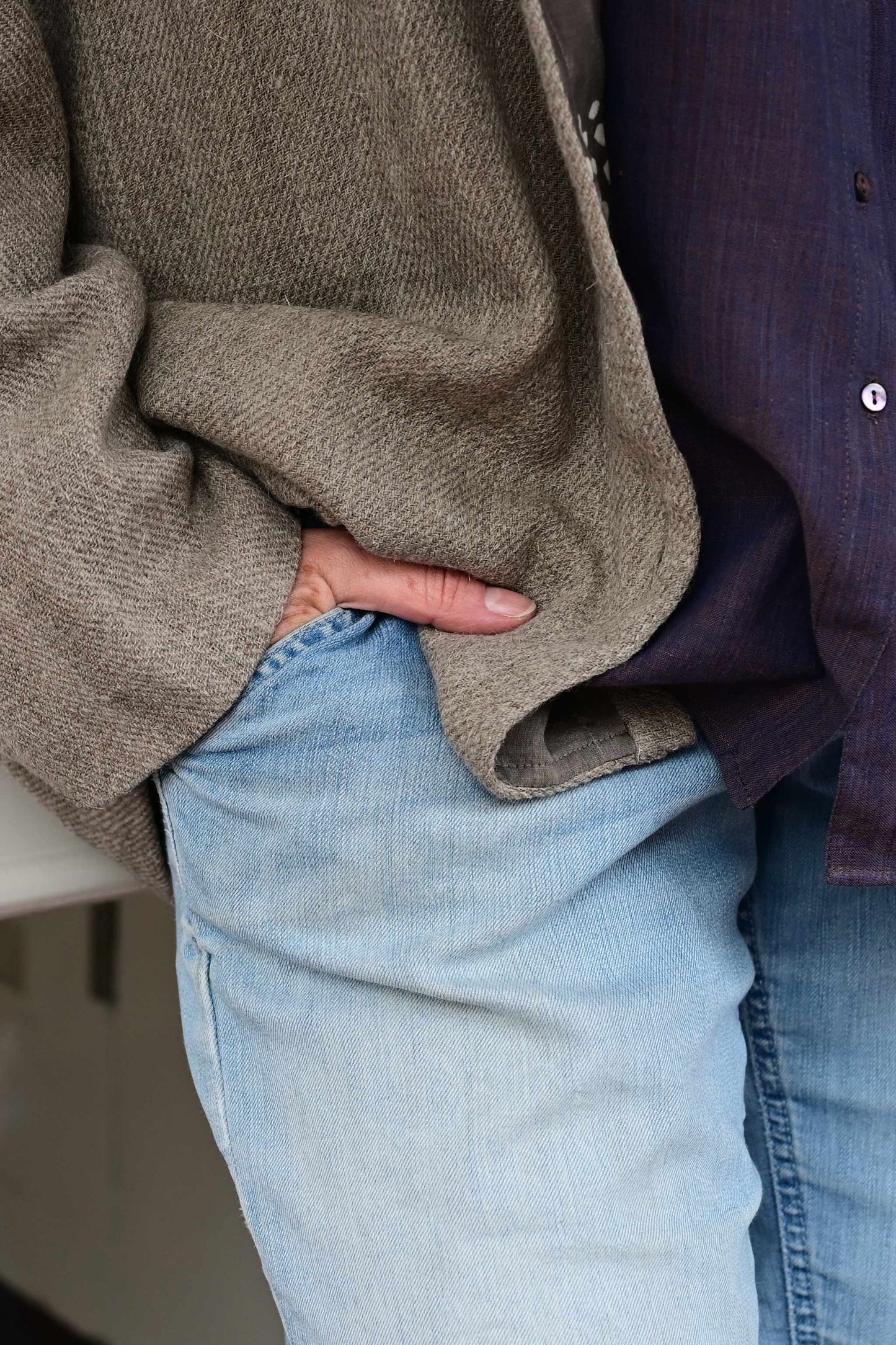 Close of the sleeve of a brown woolen jacket with hand in blue washed denims.