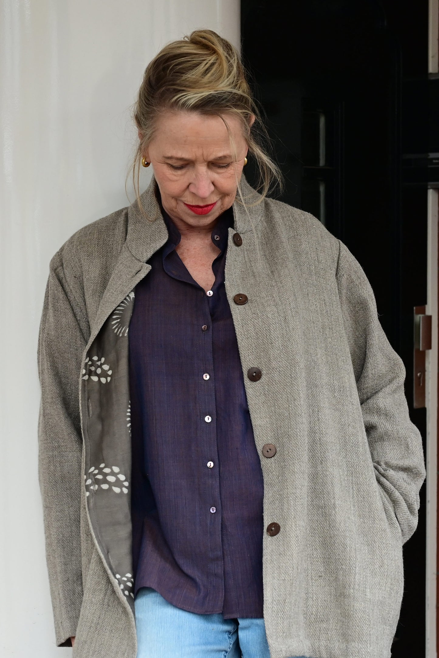 A middle aged european model looking wearing brown woolen jacket with brown hand block printed chanderi silk cotton jacket lining with buttons open. Jacket is made of handspun and handwoven Indian sheep wool by Cotton Rack.