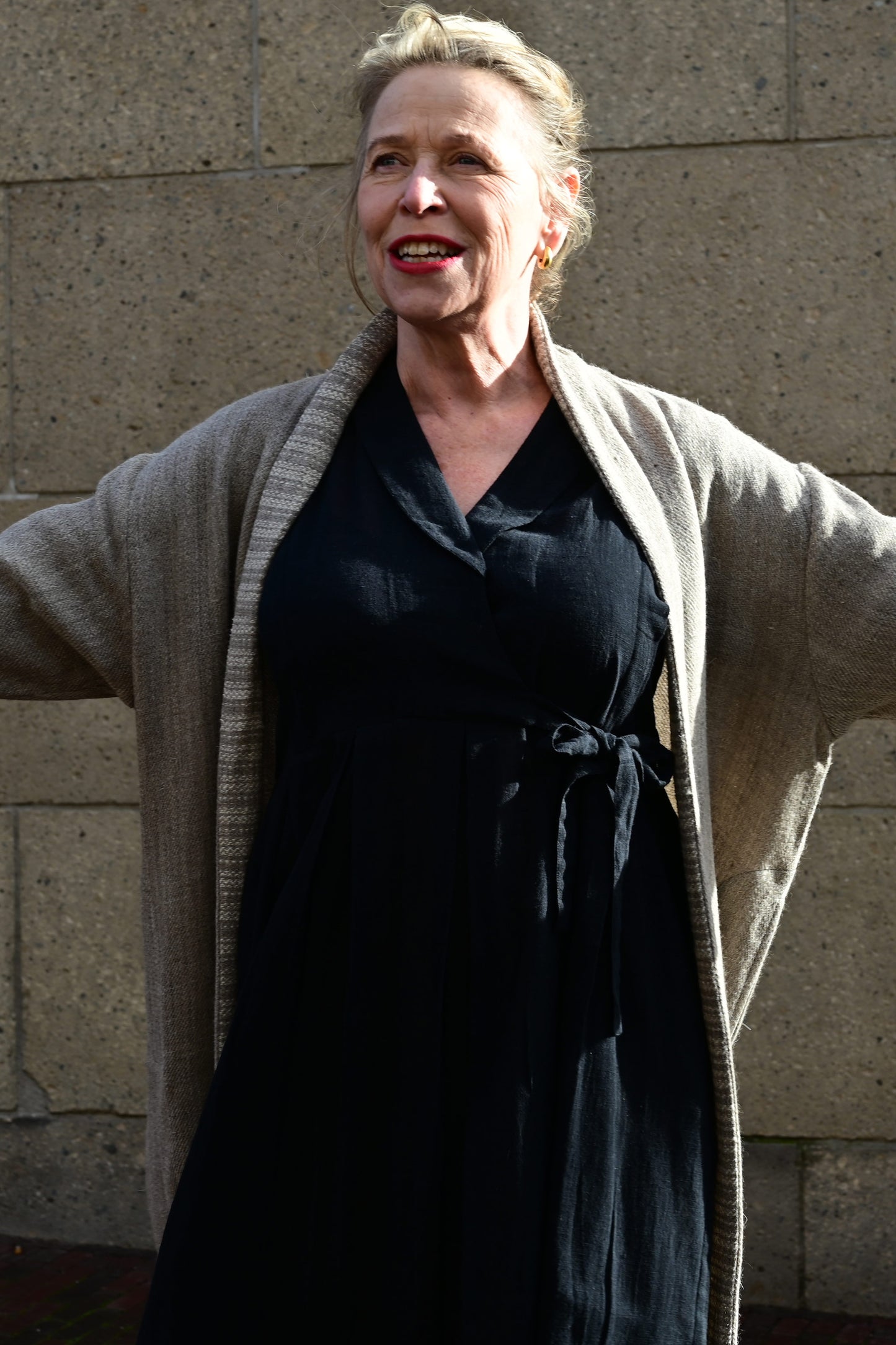 Close up of a middle aged european model posing wearing brown woolen long shrug with ivory woven pattern on the collar over a black wrap around dress. This shrug is made of handspun and handwoven Indian sheep wool by Cotton Rack.