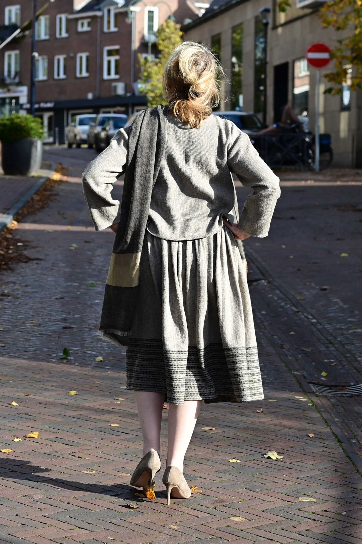 Back pose of a middle aged female model wearing a handspun handwoven khadi full sleeved crop top for ladies in natural brown wool with black details.