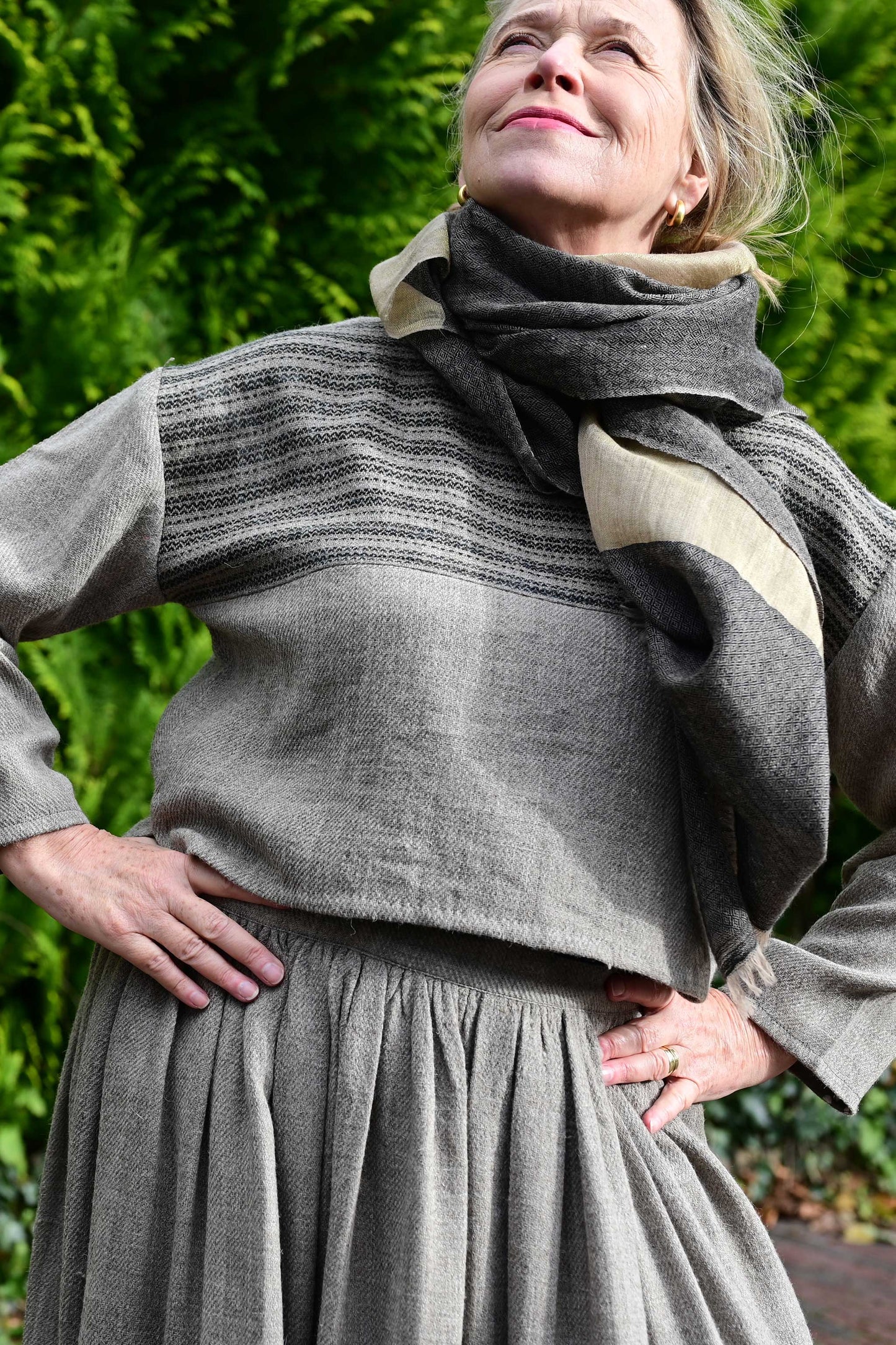 Creative front closeup of a middle aged female model wearing a handspun handwoven khadi full sleeved crop top for ladies in natural brown wool with black details.