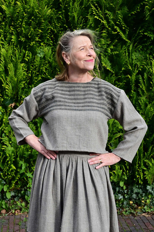 Front pose of a middle aged female model wearing a handspun handwoven khadi full sleeved crop top for ladies in natural brown wool with black details.